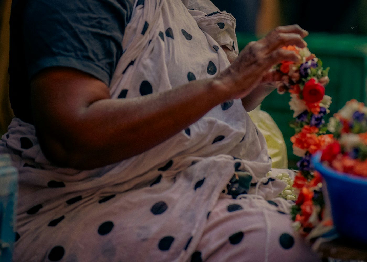 A woman threads flowers into long garlands, one after another