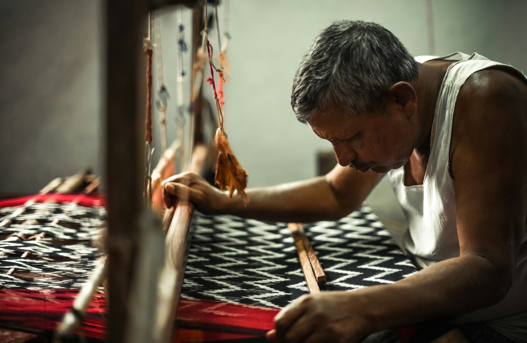 A weaver at a wooden handloom weaving black-and-white ikat fabric with red borders