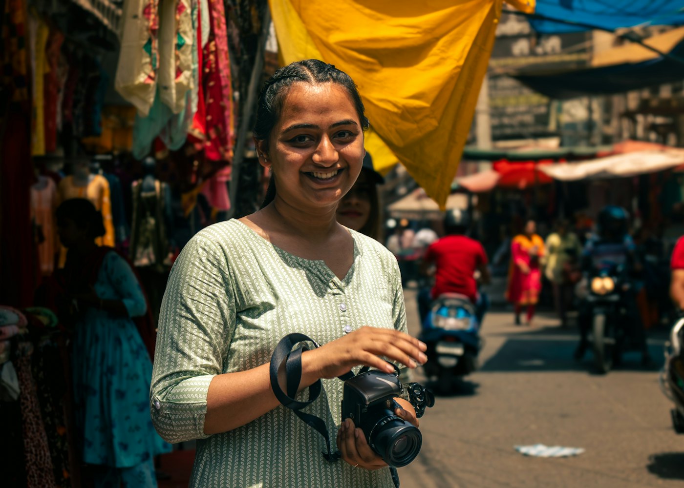 A smiling woman holding a camera in a busy market