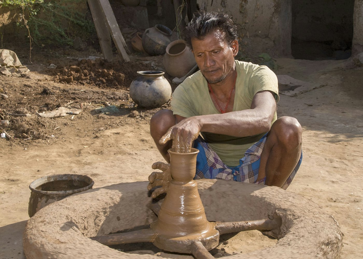A potter shapes clay on a spinning wheel outdoors