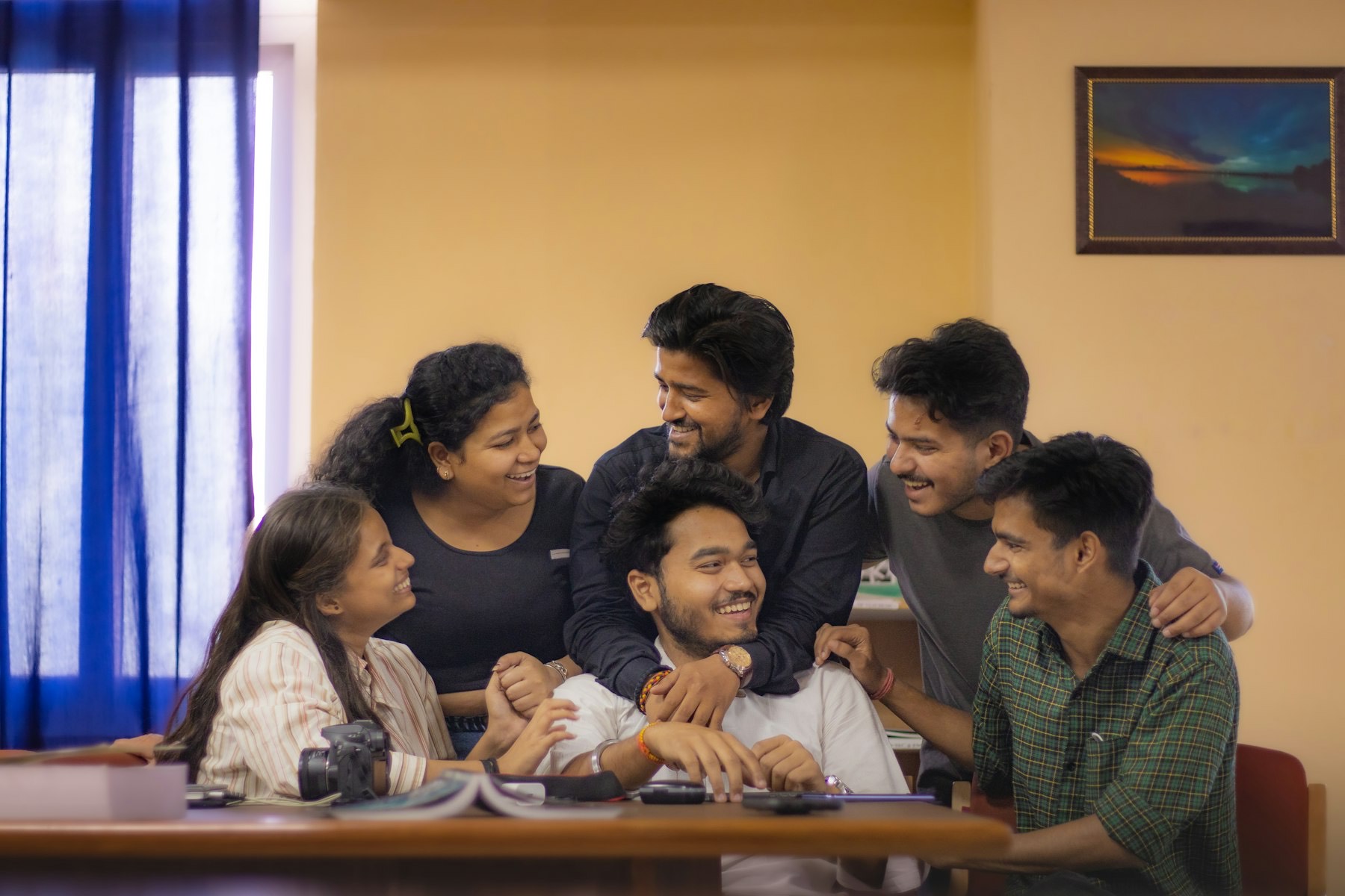 Five young colleagues laughing together around a wooden table