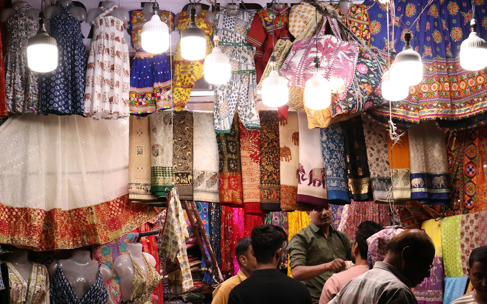 Lamp-lit clothing stall at night with fabrics hanging in rows
